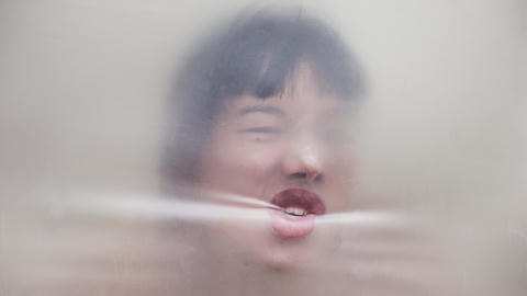 A femme face pushing up against plastic sheeting, with the mouth crimping it